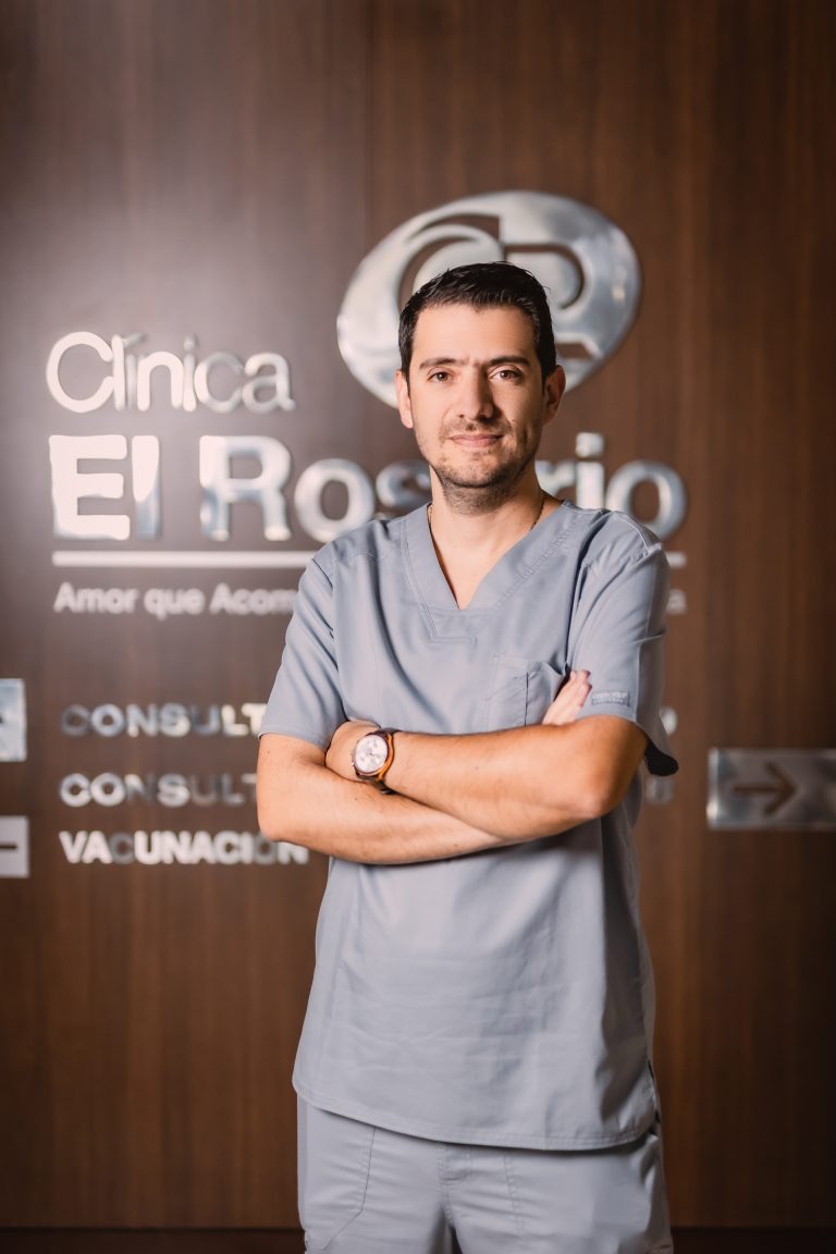El Dr. Óscar Gómez, cirujano bariátrico en Medellín, de pie frente al logo de la Clínica El Rosario